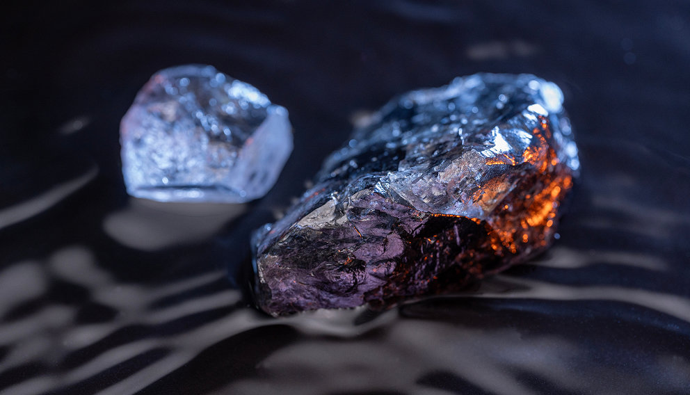 Two rough metallic mineral stones on a dark reflective surface, illuminated with blue and orange highlights